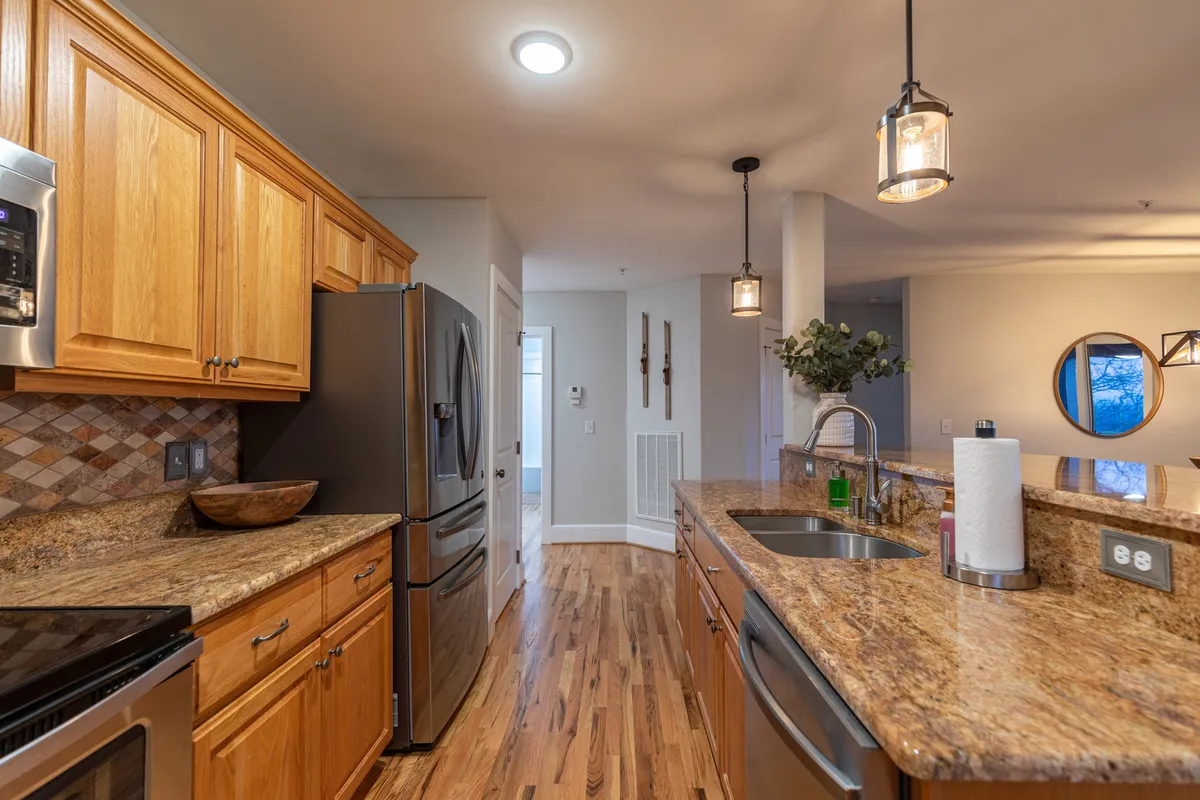 This image showcases a modern kitchen with granite countertops, stainless steel appliances, pendant lighting, and warm wooden cabinets. The space appears inviting and functional, perfect for both casual mornings and lively meal preparations.