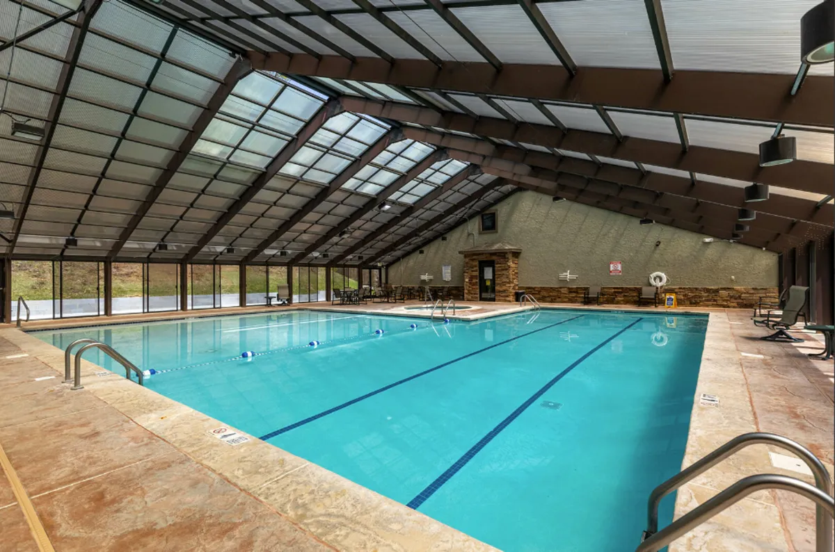 A spacious indoor swimming pool area filled with natural light from a large glass roof. Comfortable seating lines the pool, and guests are seen relaxing or swimming. The atmosphere is rejuvenating and luxurious, capturing the essence of leisure and wellness.