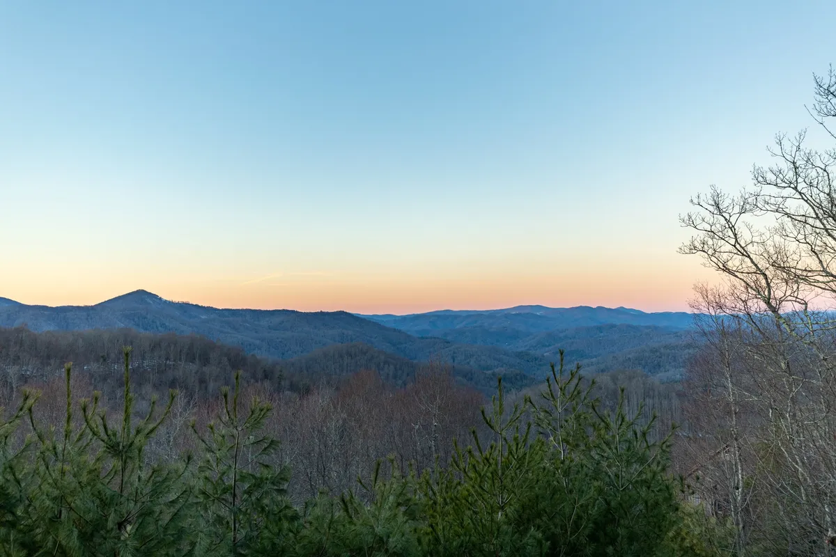 A dramatic vista of the Blue Ridge Mountains at sunset, with rich colors in the sky and lush greenery in the foreground. The image captures the serenity and grandeur of the natural setting visible from the property.