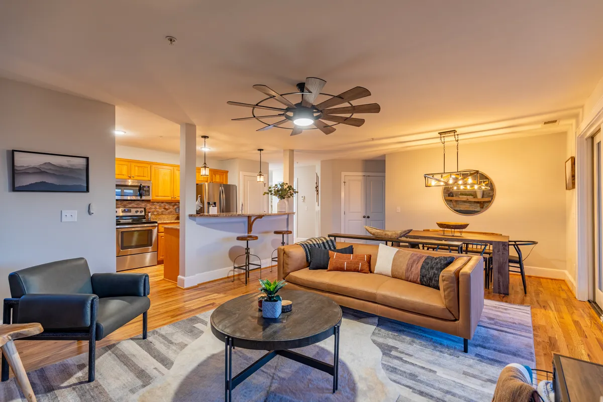 The photo captures a cozy open-concept interior that merges a plush seating area, a coffee table, a dining space, and a kitchen bar. The soft lighting and comfortable furnishings emphasize togetherness and relaxation.