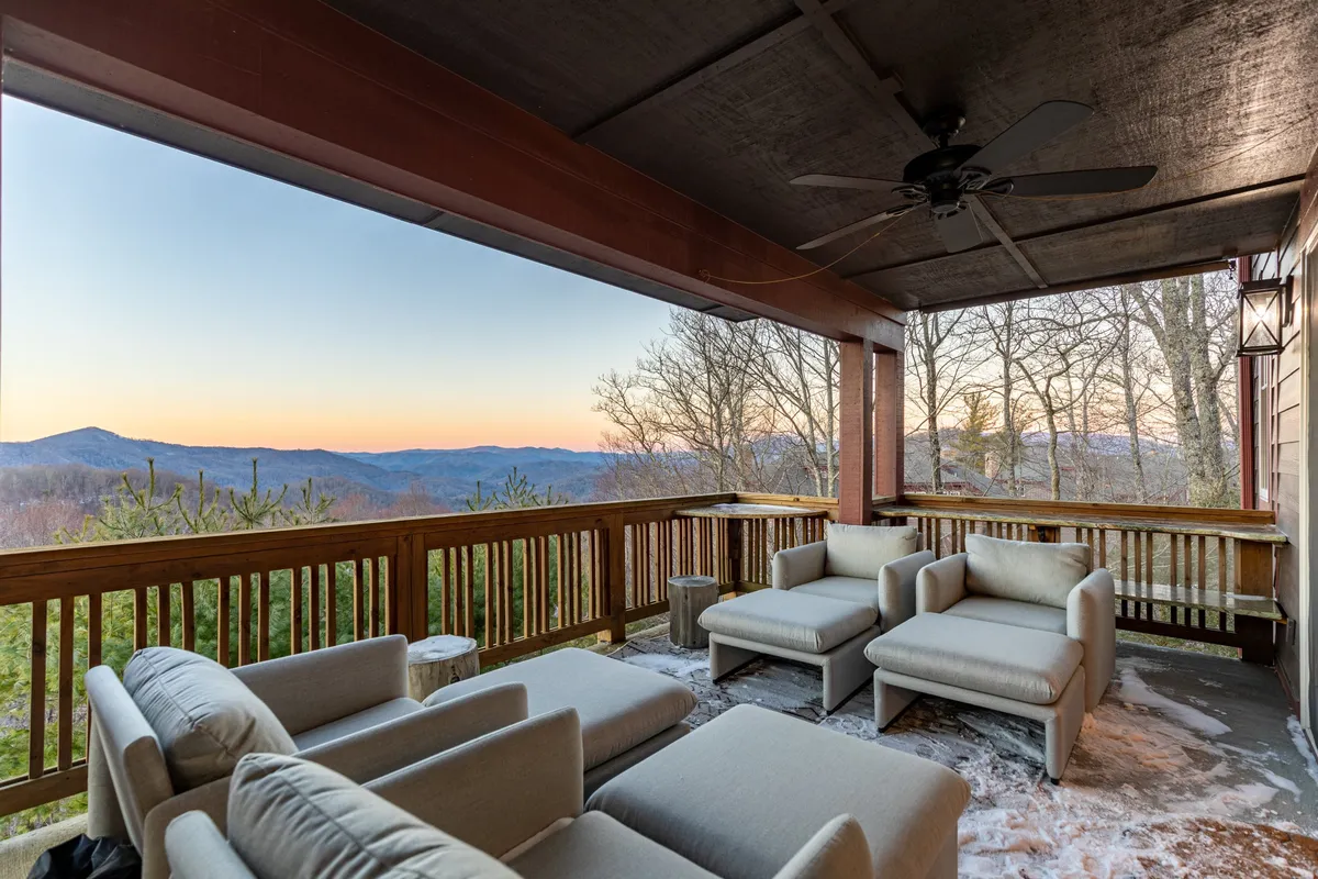 A peaceful mountain-view deck with comfortable outdoor seating and a sturdy wooden railing. The vantage point looks out onto rolling mountains, ideal for relaxing or socializing while immersed in nature's beauty.