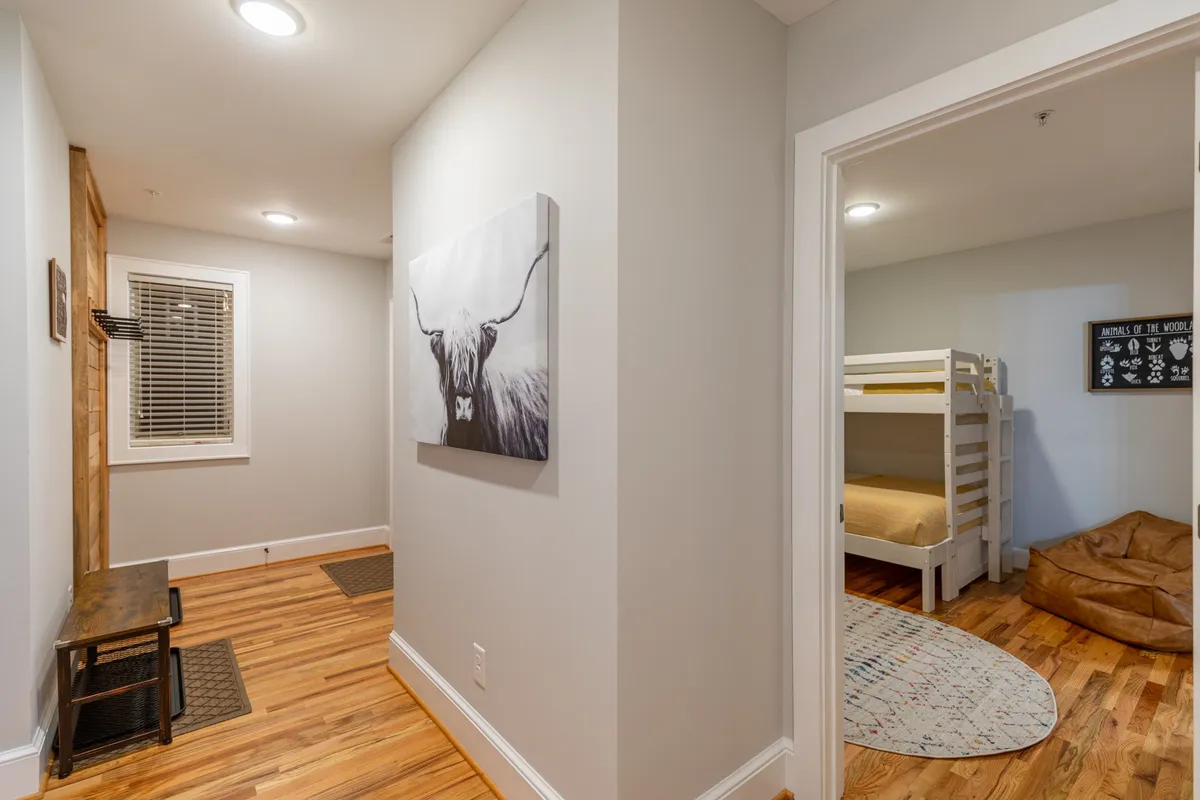 A cozy nook with large animal artwork on the wall, a wooden bench, and a glimpse into the adjacent bunk room with neatly made beds. The space feels comfortable and inviting, ideal for family game nights or quiet reflection.